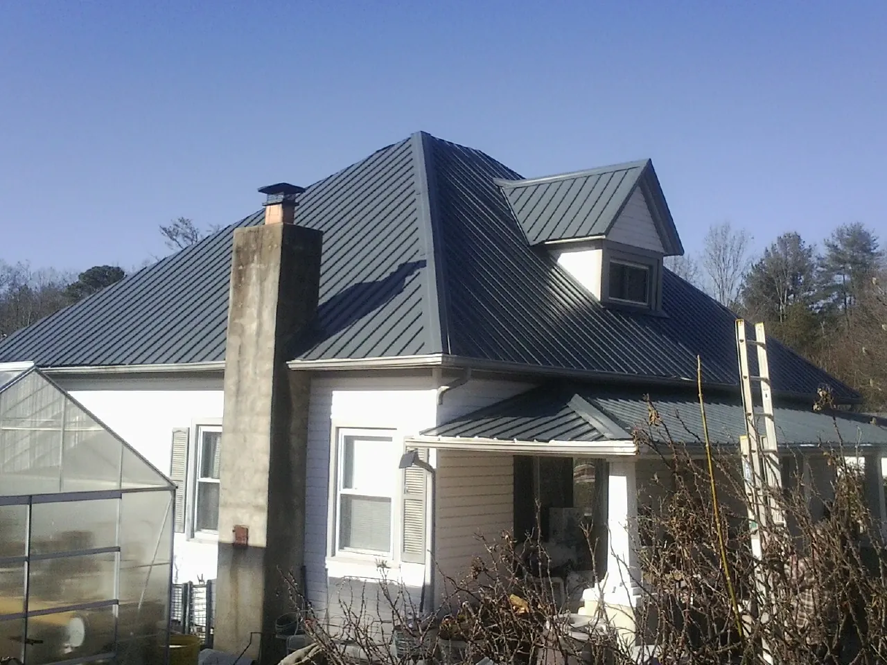 Dark blue standing seam metal roof on a white farmhouse with dormer — Slate & Tile Roof Repair by Roofing Brothers in La Belle