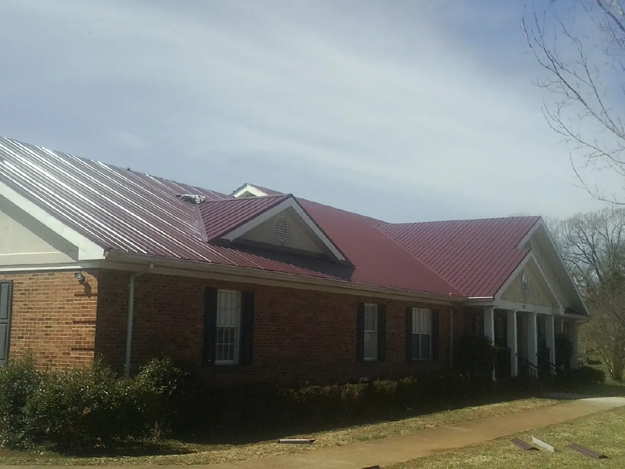Red metal roof with gabled entries on a long brick building, from a Hail Damage Roof Repair job in La Belle