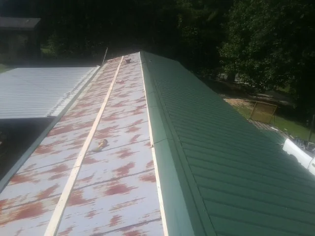 Old rusted panels beside newly installed green metal roofing — Wind Damage Roof Repair by Roofing Brothers in La Belle