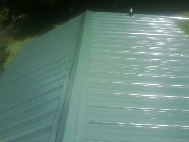 New green metal panels meeting at the ridge of a roof — Flat Roof Repair work by our crew in La Belle