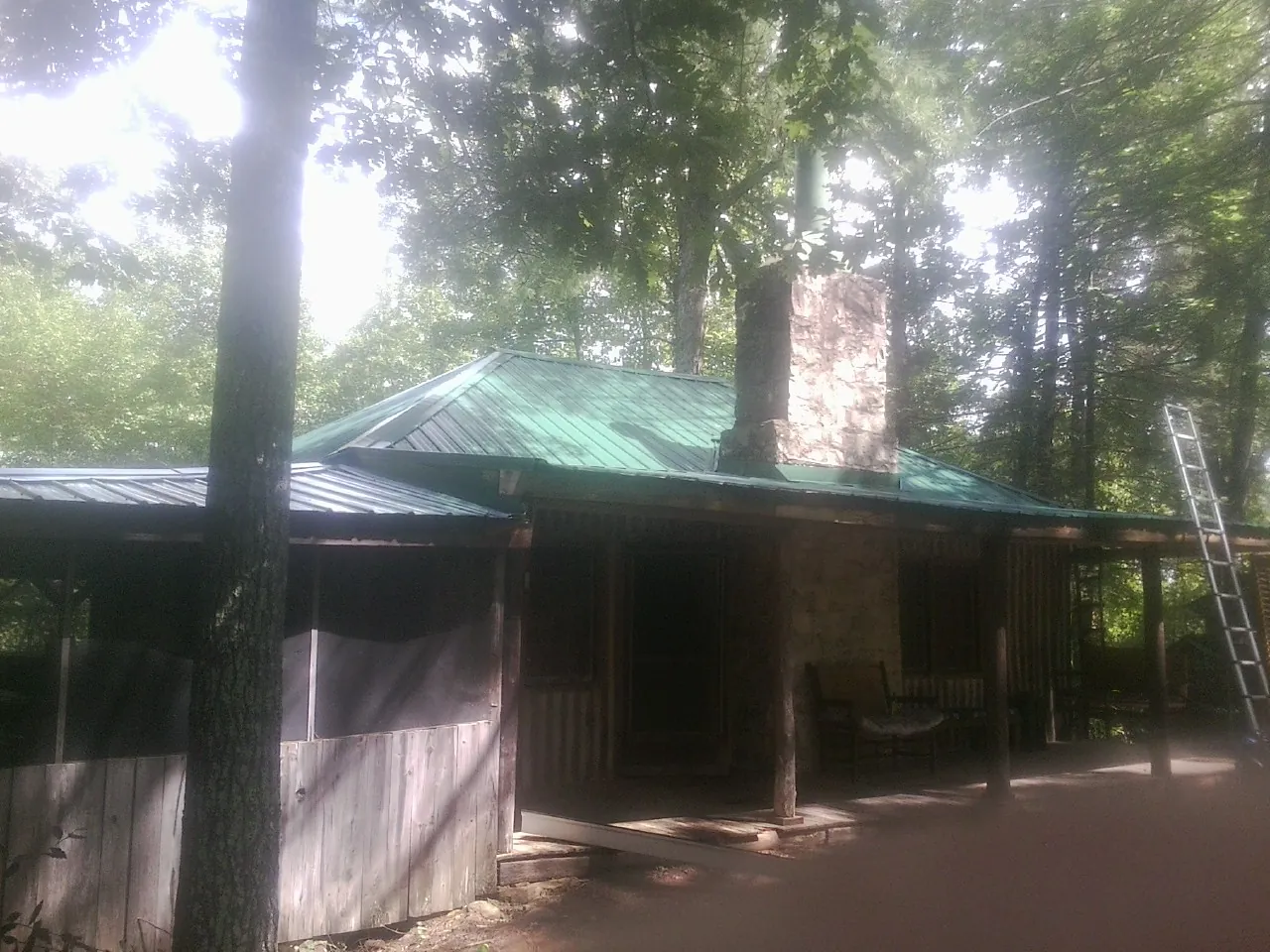 Green metal roof and stone chimney above a log cabin porch in La Belle