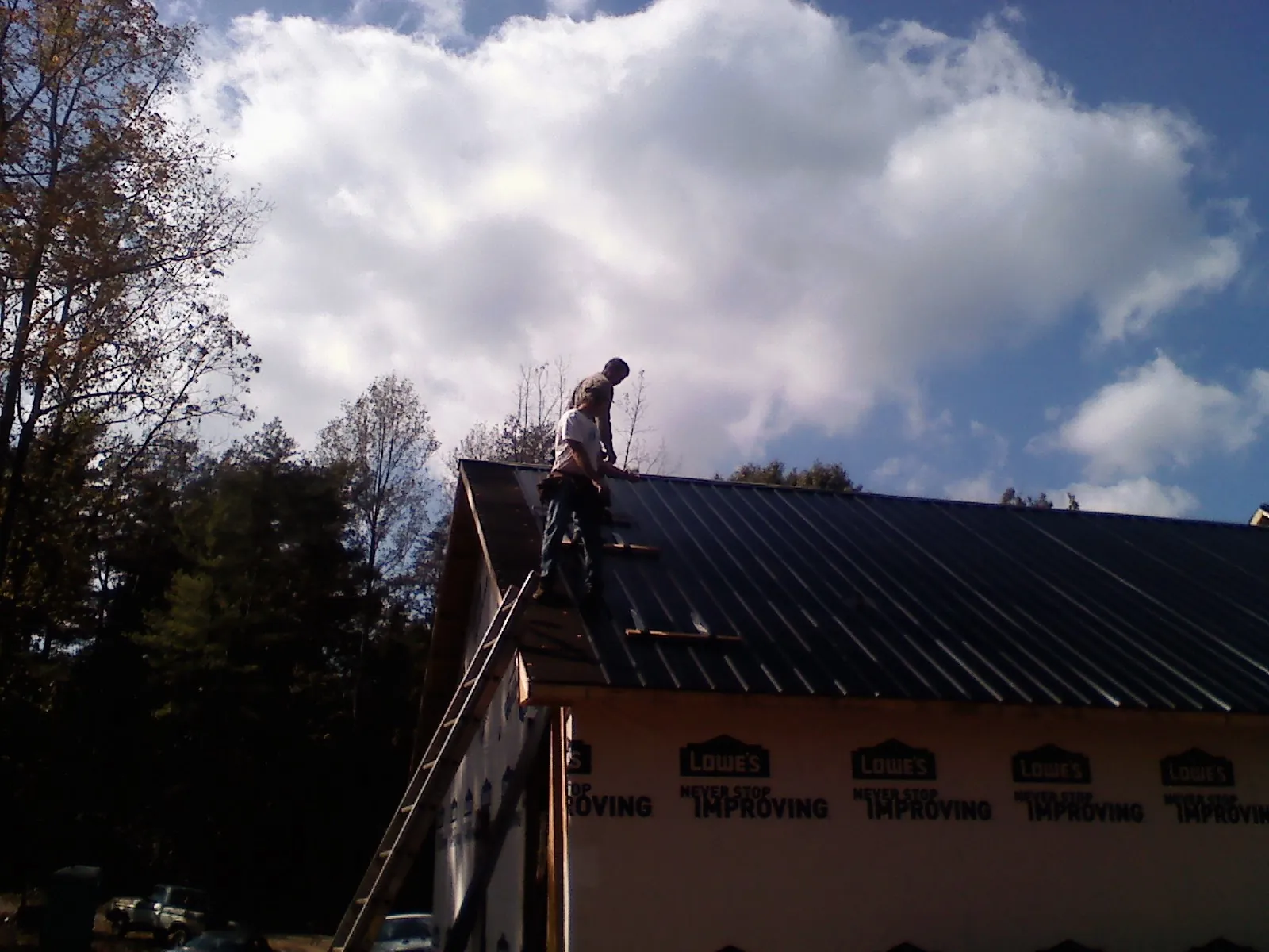 Roofer fastening dark metal panels high against a cloudy sky, from a Roof Inspection job in La Belle
