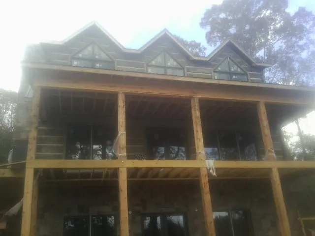 Dormers and porch framing on a large log home under construction — Roof Coating work by our crew in La Belle
