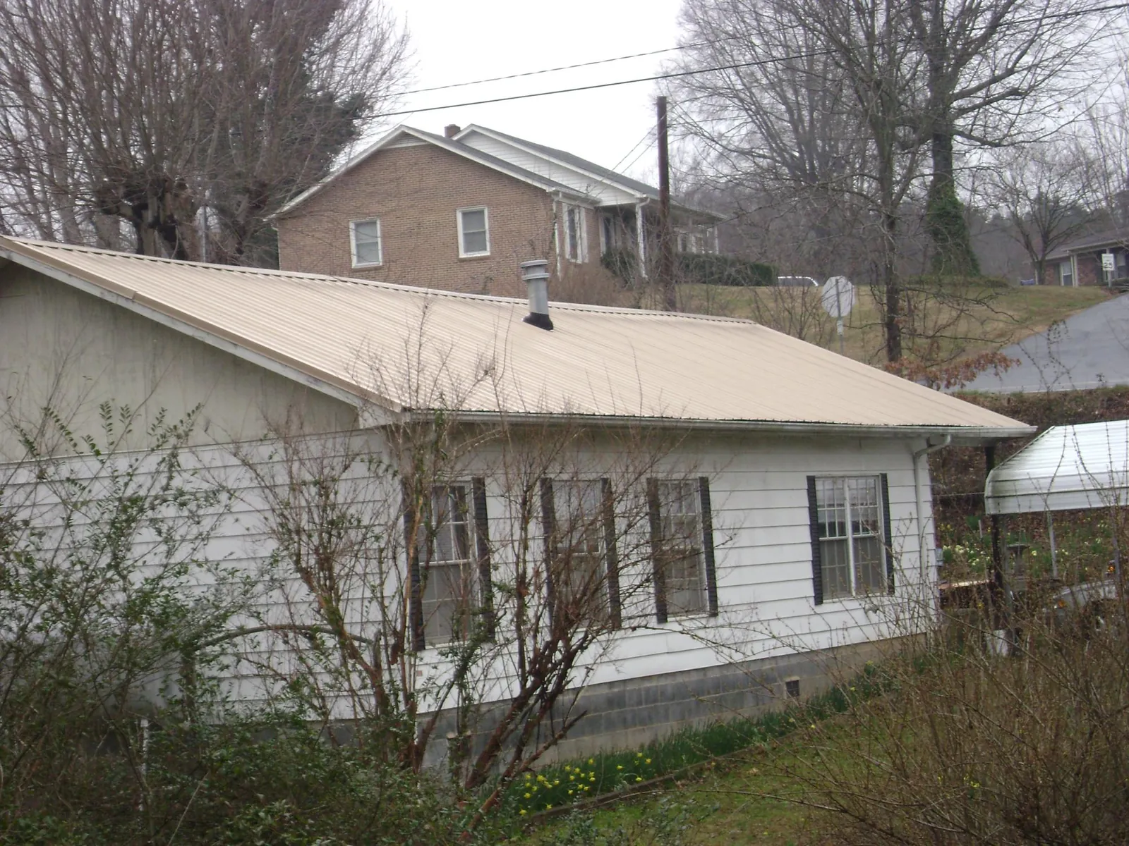 Tan metal roof on a white sided house set into a hillside — Commercial Roofing by Roofing Brothers in La Belle