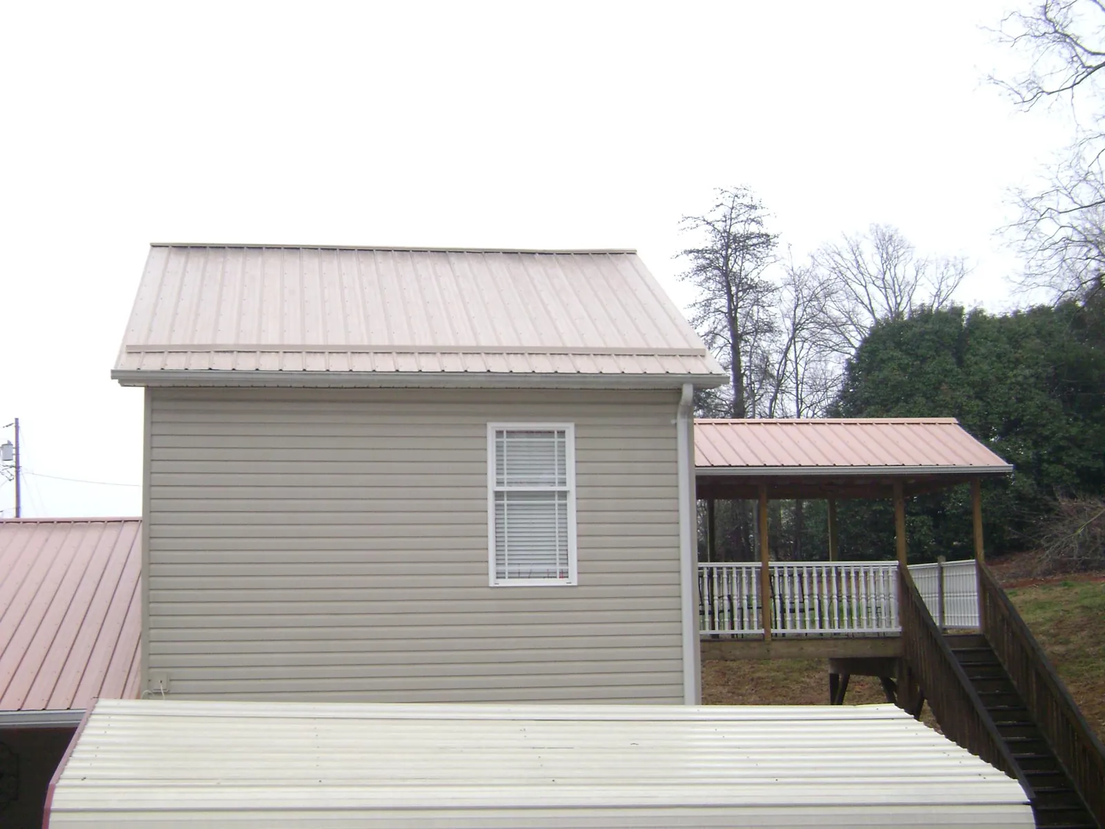 Tan metal roofs on a two story addition and attached porch, from a Roof Replacement job in La Belle